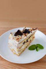 Vanilla sponge cake biscuit with prune, walnuts and frosting served on a white plate, on light wooden background table