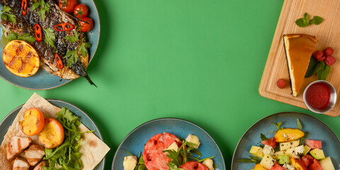 Holiday celebration table setting with food. Flat-lay of sweet cheesecake, fruit salad, meat dishes. Copy space banner.