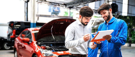 Mechanic show the car checking list for customer with blur his assistant checking red car. Focus on mechanic and customer on the right side. Auto car repair service center. Professional service.