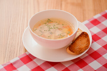 Chicken soup with vegetables and meat served in a white bowl over rustic wooden background with red plaid tablecloth.