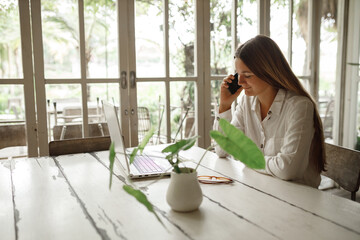 Woman using laptop in cafe.Girl sitting at a cafe,laughing and enjoying at coffee, talking by the phone