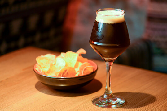 Glass of dark beer with chips on the counter table in bar. Alcohol drink. Food photography concept, copy space.