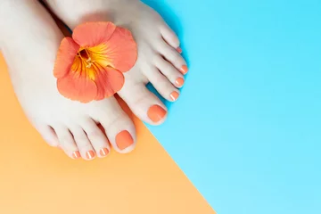 Poster Weibliche Beine mit einer schönen orangefarbenen Pediküre mit Blume auf blauem und orangefarbenem Hintergrund © TATIANA