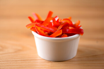 Red sweet peper in a small bowl, isolated on light wooden table background.