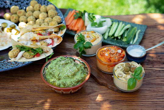 Vegetarian picnic on a wooden oak table, hummus, falafel, pita, vegetables, spinach, basil and sunflower seed pesto sauce. Healthy Mediterranean food.