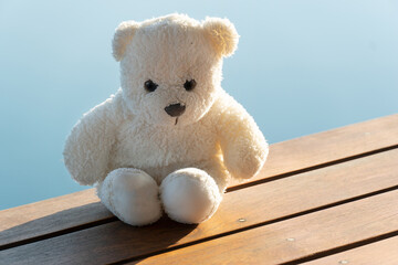 angry white bear doll sitting on terrace with outdoor blue nature water and sunlight