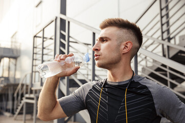 Image of unshaven caucasian sportsman drinking water while working out