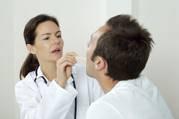 Obraz na płótnie Canvas Female doctor using tongue depressor to examine her patient