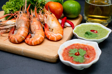 Close up of fresh grilled shrimp served on a wooden plate with sauce, onions, garlic and chilies