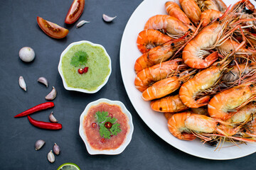 Top view of cooked river prawns served with fresh chilies, garlic, lemons and tomatoes on a gray stone floor.