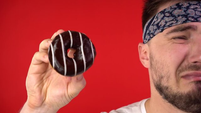 Close-up of a man with dark hair. A man holds a glazed donut in his hands, a man is upset, almost crying, can not resist, he wants to bite a donut. Sweet tooth man, addiction to sweets.
