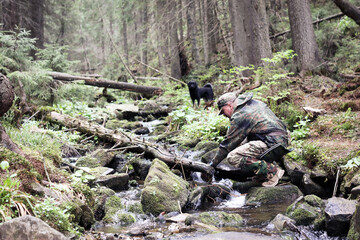 hikers man taking clear water from rill in forest