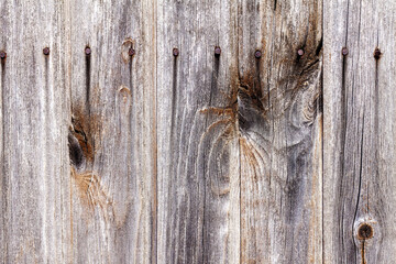 Background of gray and brown wooden fence from boards with traces of knots and rusty nails in the upper half of the image