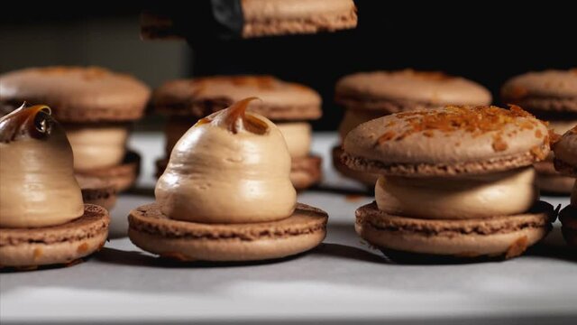 Chef is assembling caramel macarons. Close-up of hand in glove is puts a shells on french cookies.