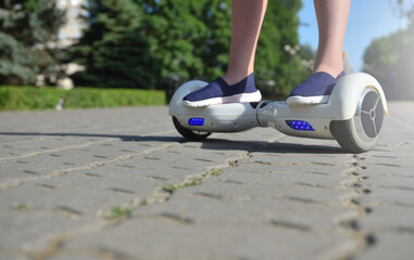 Electric hoverboard and legs of a girl child on a background of a summer park