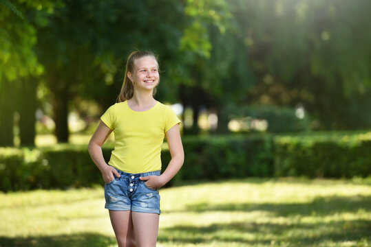 Happy girl child in a yellow T-shirt and denim shorts on a background of  green trees Stock Photo | Adobe Stock