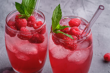 Fresh ice cold berry juice drink with mint, summer raspberry lemonade in two glass with straws on stone concrete background, angle view macro