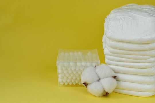 Baby diapers with cotton buds and dried cotton on yellow with copy space.
