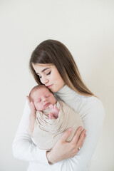 Happy young mother with dark hair holds a baby in her arms in a beige diaper. Happy motherhood