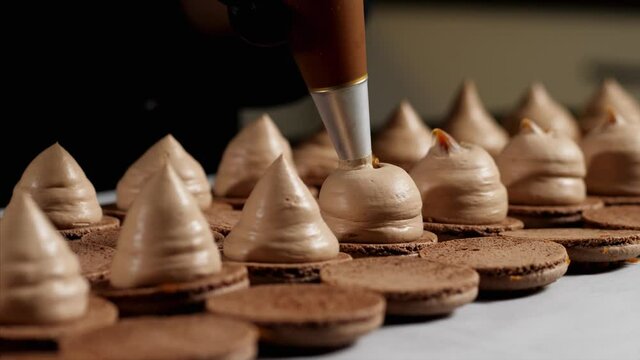 Chef is making caramel macarons. Hand with confectionery bag squeezing caramel in cream filling, close-up.