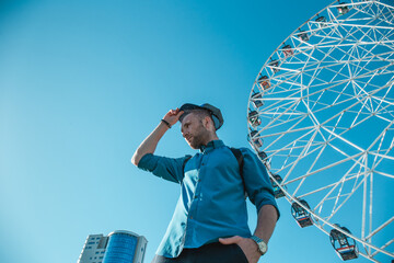 Young man in the city on a background of blue sky and ferris wheels. Space for text.