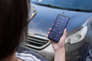 Smart car app concept on smart phone in woman hand with car status information. Modern car in...