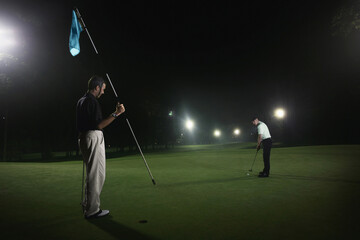 Two men playing golf at night