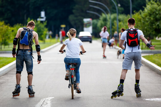 A girl rides a bicycle and next to her two guys on roller skates