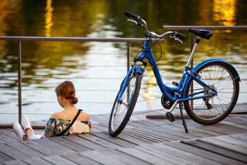A girl reads a book on the on the lake embankment near the bike
