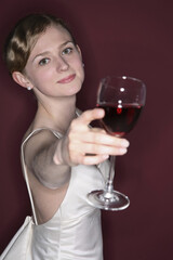 Woman in wedding gown extending a glass of red wine