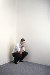 Businessman squatting down in corner of room