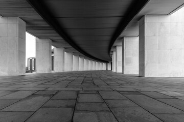 A smoothly curved gallery with rectangular vertical light columns of stone. Dark ceiling and floor. A distant perspective. Black and white image.