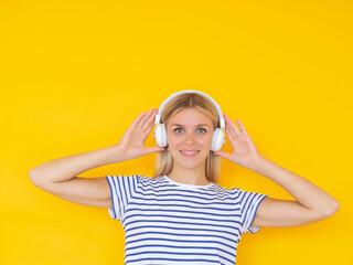 Music lifestyle concept. Smiling girl looking at camera while touching white wireless headphones on yellow background