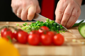 Close up of man cutting green fresh onion for salad in the kitchen at home. Cooking recipes concept