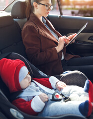 Mother with her small child in a baby car seat ride in the back seat of a taxi