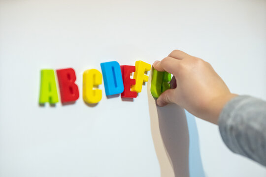 Close-up Of Child Hand Sticking Letter Magnets On Wall