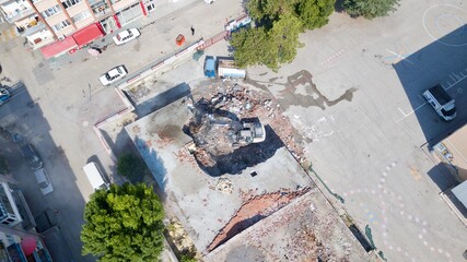 Aerial view of excavator demolishes an old building in city center. Water truck squeezes water to...