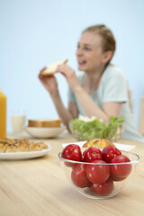 A bowl of tomatoes with woman having breakfast in the background