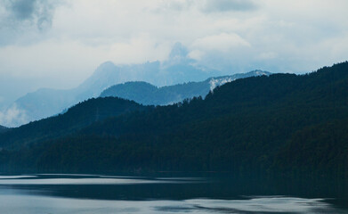 Berggipel in Wolken und regenverhangenem  Himmel mit See im Vordergrund