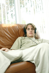 Teenage boy sitting on the couch listening to music on the headphones