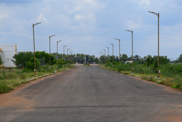 deserted lonely wide road due to pandemic lockdown with beautiful sky and street lamp post aligned perspective, symmetrical during day time in Central University of Tamil Nadu, India 