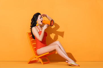 attractive woman in swimwear holding megaphone and screaming while sitting on deck chair on orange
