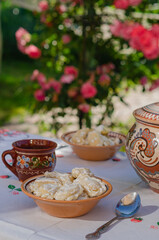 Homemade pierogi in clay ethnic Ukrainian dishes on a table in the summer garden.