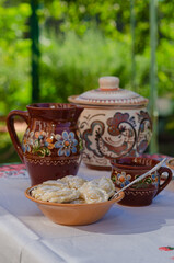 Homemade pierogi in clay ethnic Ukrainian dishes on a table in the summer garden.