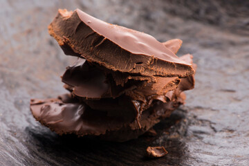 Heap of broken pieces of bitter or milk chocolate scattered on dark background