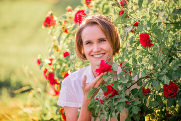 Obraz na płótnie Canvas portrait of a young woman among red roses in the back sunlight