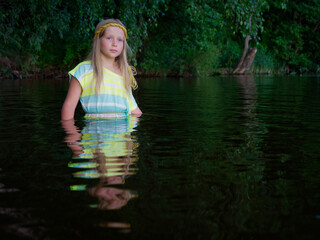 blonde girls with blue eyes bathes in clothes in the dark water of a lake at sunset