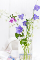 Bouquet of wild flower bellflower campanula , in a glass vase on an embroidered tablecloth in white wooden background, home decoration concept