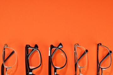 Different types of glasses on an orange background close up. Glasses with rectangular and round frames. Layout for design. Space for text and free space near the object.