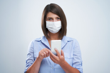 Attractive woman wearing protective mask holding smartphone isolated over white background